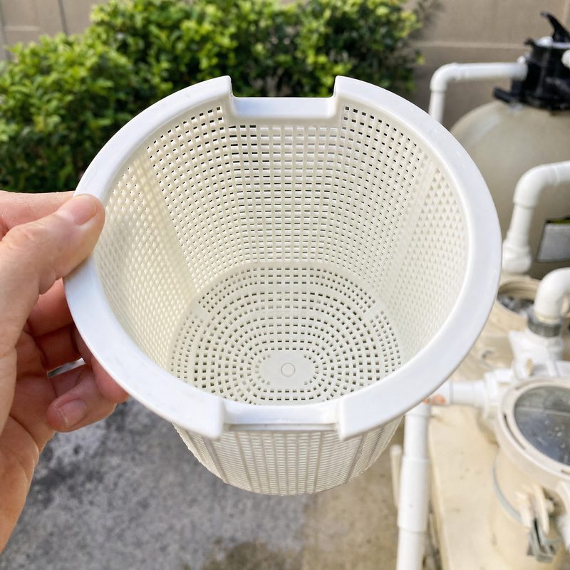 An emptied skimmer basket held up in front of the equipment pad.